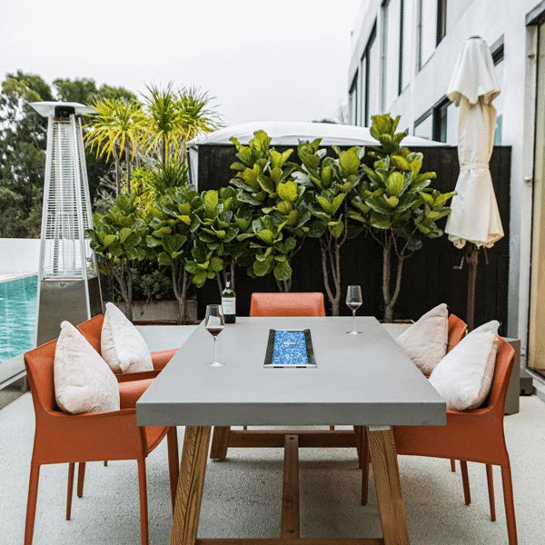 rectangular outdoor dining table with fire pit. fire pit is not lit but has fire glass laid out. table is set beside the pool in a backyard