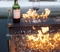 square fire pit table lit on fire glass and wind screen surrounding fire pit with wine bottle and glass set out on fire table