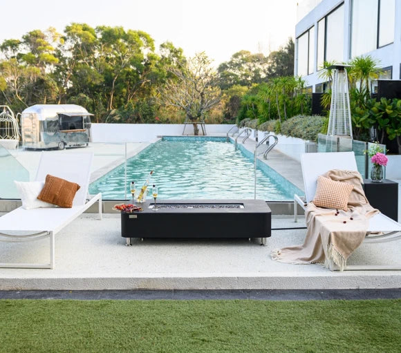 black rectangular fire pit coffee table in between two sun loungers and behind swimming pool