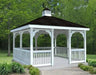 White vinyl gazebo with a double roof and a cupola. The gazebo has a rectangular shape with a gabled roof and white railings. The gazebo is surrounded by green trees and grass.