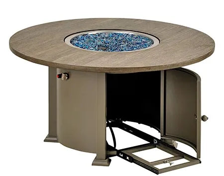  A round outdoor fire table with a granite top and a black metal base. The table has a circular burner and a control panel with a knob and a switch. A granite lid covers the burner, and a door on the side of the base reveals a storage compartment.