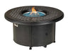 A round outdoor fire pit table with a black metal frame and a circular burner. Blue flames are visible through the decorative metal grate. There is a propane tank storage compartment at the base, and the table has four small wheels.