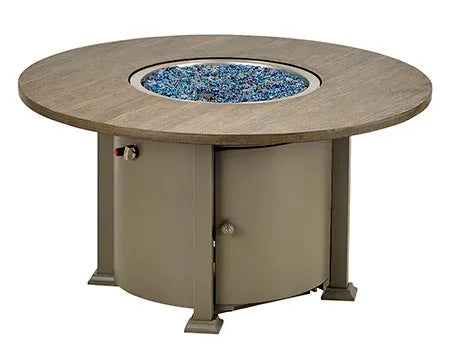 A round outdoor fire table with a granite top and a black metal base. The table has a circular burner and a control panel with a knob and a switch. A granite lid covers the burner, and a door on the side of the base reveals a storage compartment.