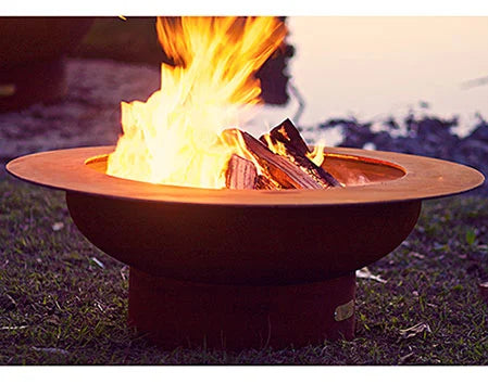 Wood burning fire pit with a roaring fire. The fire pit is round and made of rusted metal. The flames are orange and yellow and are rising high into the air.