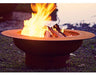 Wood burning fire pit with a roaring fire. The fire pit is round and made of rusted metal. The flames are orange and yellow and are rising high into the air.