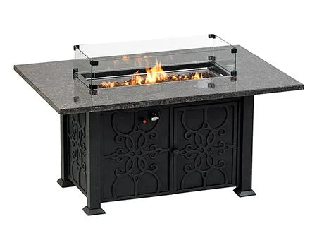 A rectangular outdoor fire table with a granite top and a black metal base. The table has a glass wind guard and burning flames inside.