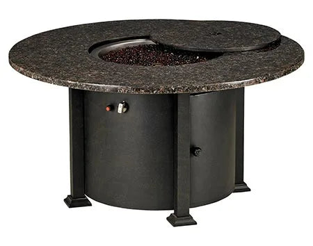  A round fire pit table with a granite top and a black metal base. The table has a circular burner and a control panel with a knob and a switch. A granite lid covers the burner, and a door on the side of the base reveals a storage compartment.