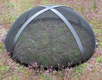 A black metal spark guard with a domed top and four handles. The spark guard is placed on a bed of purple flowers.