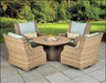 A patio furniture set made of wicker with a circular fire pit table in the center. The set includes four swivel chairs with light blue cushions. The fire pit table has a bronze-colored base and a glass top with blue flames visible. The background shows a green lawn and trees.