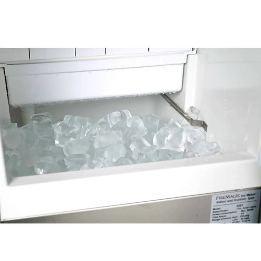 A close-up of the interior of a Fire Magic Outdoor Ice Maker. The ice bin is filled with a large quantity of clear, bell-shaped ice cubes.