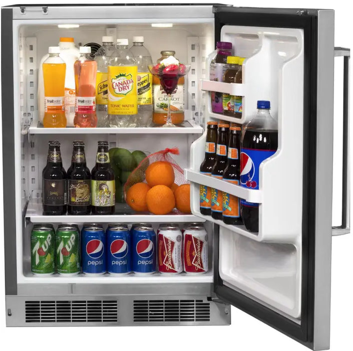 A stainless steel Fire Magic outdoor refrigerator with the door open, revealing the interior. The refrigerator is stocked with various beverages and snacks, including bottles of soda, beer, juice, and cans of soda. There are also fruits like oranges and limes.