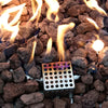 Close-up of flames and lava rocks with a perforated metal ignition box glowing from the heat.
