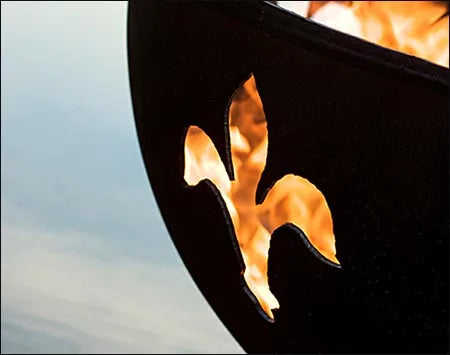 A close-up of a fleur-de-lis cutout in a black fire pit, with flames visible through the cutout.