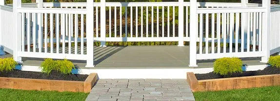 A close-up shot of a white vinyl gazebo with white railings and a gray composite gazebo floor kit, showing a stone pathway leading to the gazebo