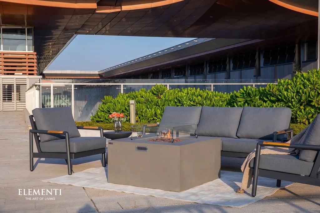 Outdoor patio set with gray chairs and sofa around a square fire pit coffee table on a wooden deck.