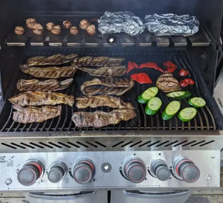 A grill filled with a delicious spread of grilling options, from juicy steaks and veggies to warm potatoes.