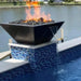 Black metal HPC Fire's Sedona fire pit with water bowl in a stainless steel mesh screen and a log grate. Sits on a black metal stand with four legs.