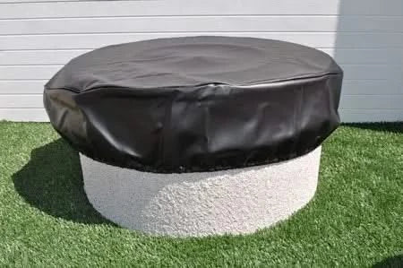 A black plastic cover sits on a round table with a white pillow on top. The text on the cover says "HPC Fire Pit Cover" and "HPC Round Vinyl Fire Pit Cover 35". There is a blurred image of fire pit covers in the background.