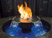 A black, circular fire pit with a water fountain in the center. The fire pit has a metal fire ring and a stainless steel base. The water fountain has a fire burning on top of the water. The fire pit is surrounded by black lava rocks.