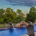 Outdoor pool area with fire pit and water feature, surrounded by trees and a fence.