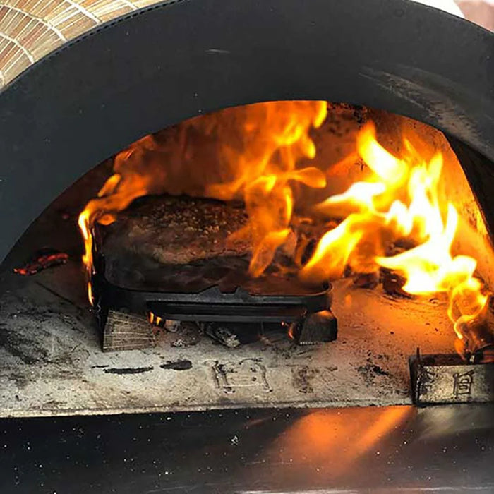 A juicy steak with grill marks being seared in a brick oven. Flames are visible through the glass window of the oven door. The oven is built into a stone structure with a stainless steel countertop.