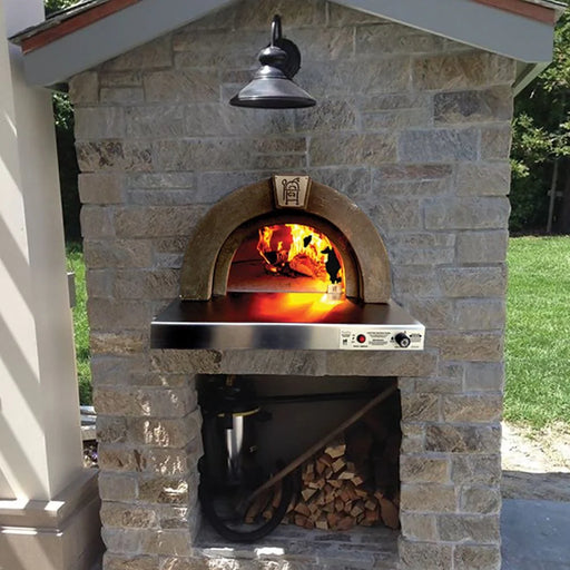 A brick pizza oven with a fire burning inside. The oven has a stainless steel base and is sitting on a brick wall. The oven is surrounded by a stone wall.