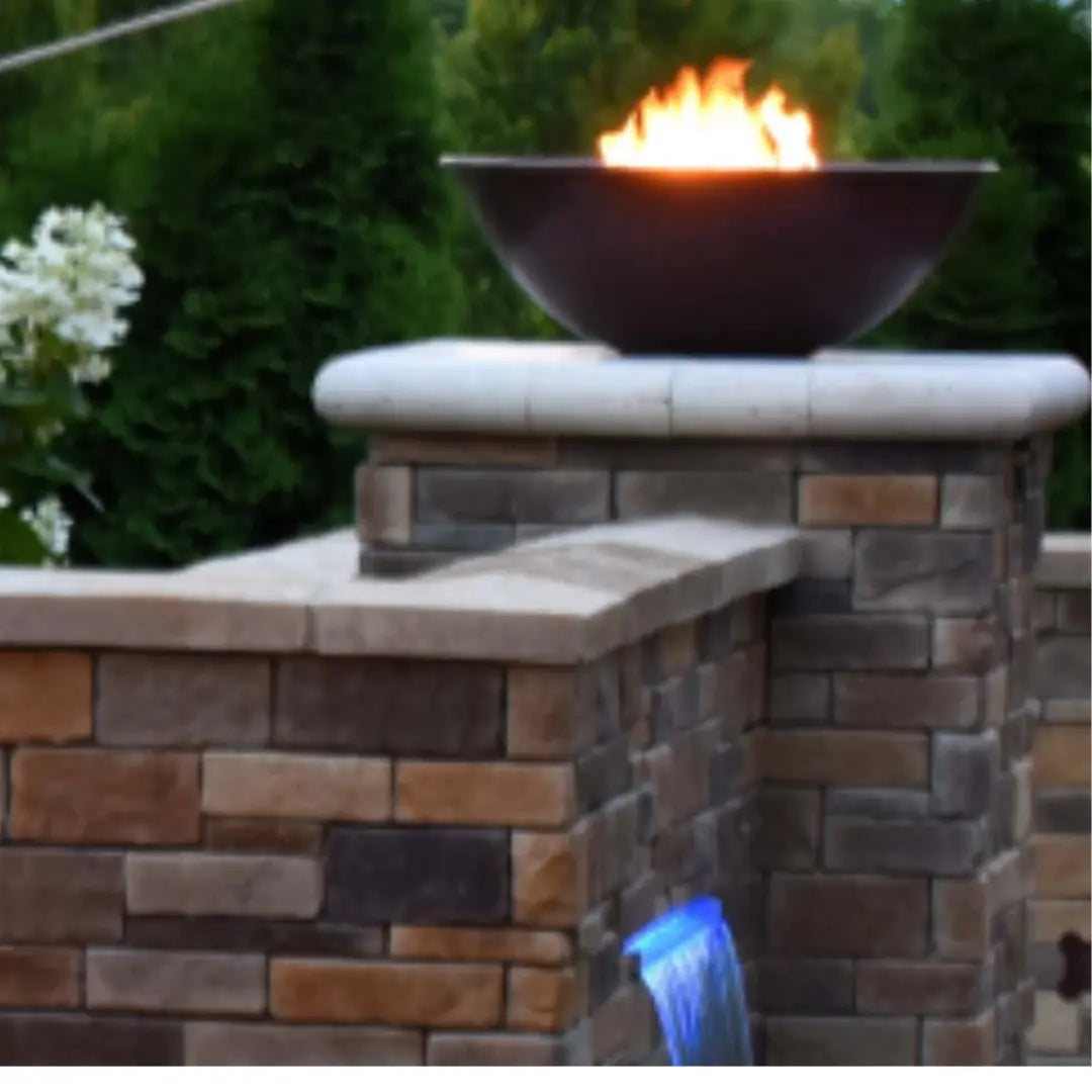Mesa copper fire bowl with flames on outdoor stone pillar wall in backyard garden setting at dusk