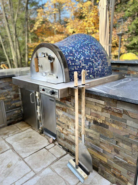 HPC Villa Series Built-In Outdoor Pizza Oven. The oven is stainless steel with a glass tile front and sits on top of a stainless steel countertop. The brochure text highlights the oven's features, including electronic ignition, dual-fuel capability (gas and wood), and a 304 stainless steel hearth.