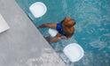 man with a bottle in his hand sitting on white bar height pool stool n the edge of a swimming pool