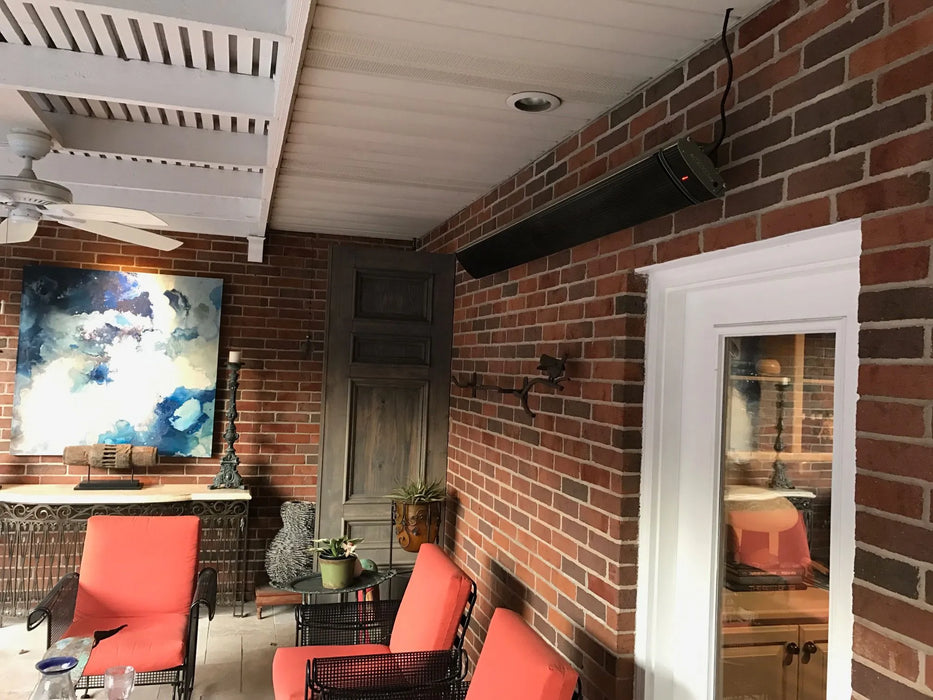 Electric patio heater installed on a brick wall, providing warmth to a cozy outdoor seating area with red chairs and a ceiling fan.