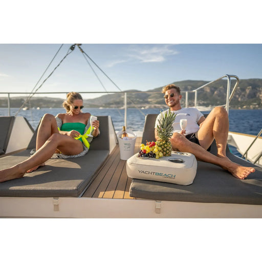 Two people on a boat with a Yacht Beach branded cooler and inflatable beverage holder