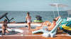 People enjoying a day at the beach with a boat and water toys on top a large inflatable platform