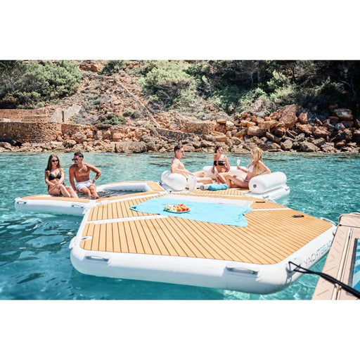People relaxing on a floating swim platform in a scenic location with trees and rocks.