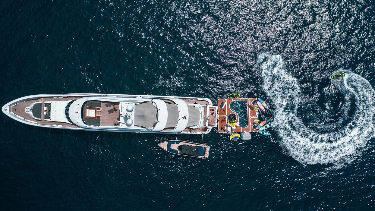 Aerial view of a large yacht with smaller boats on a dark blue ocean.
