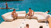 People relaxing on inflatable furniture by a body of water with a person paddleboarding.