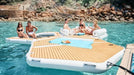 People enjoying a floating yacht platform in a scenic water setting with rocky shores.