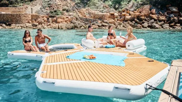 People enjoying a floating yacht platform in a scenic water setting with rocky shores.