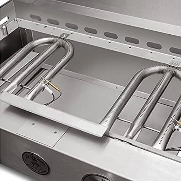 A close-up of the underside of a stainless steel gas griddle. Two U-shaped burners are visible, along with gas lines and connectors.