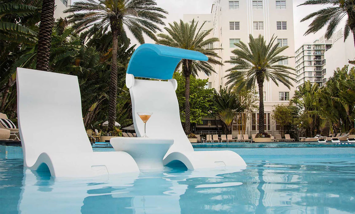 Two Ledge Lounger Signature Pool Chairs with a small table in between, showcasing their use in a relaxing poolside setting with palm trees and a cityscape in the background.