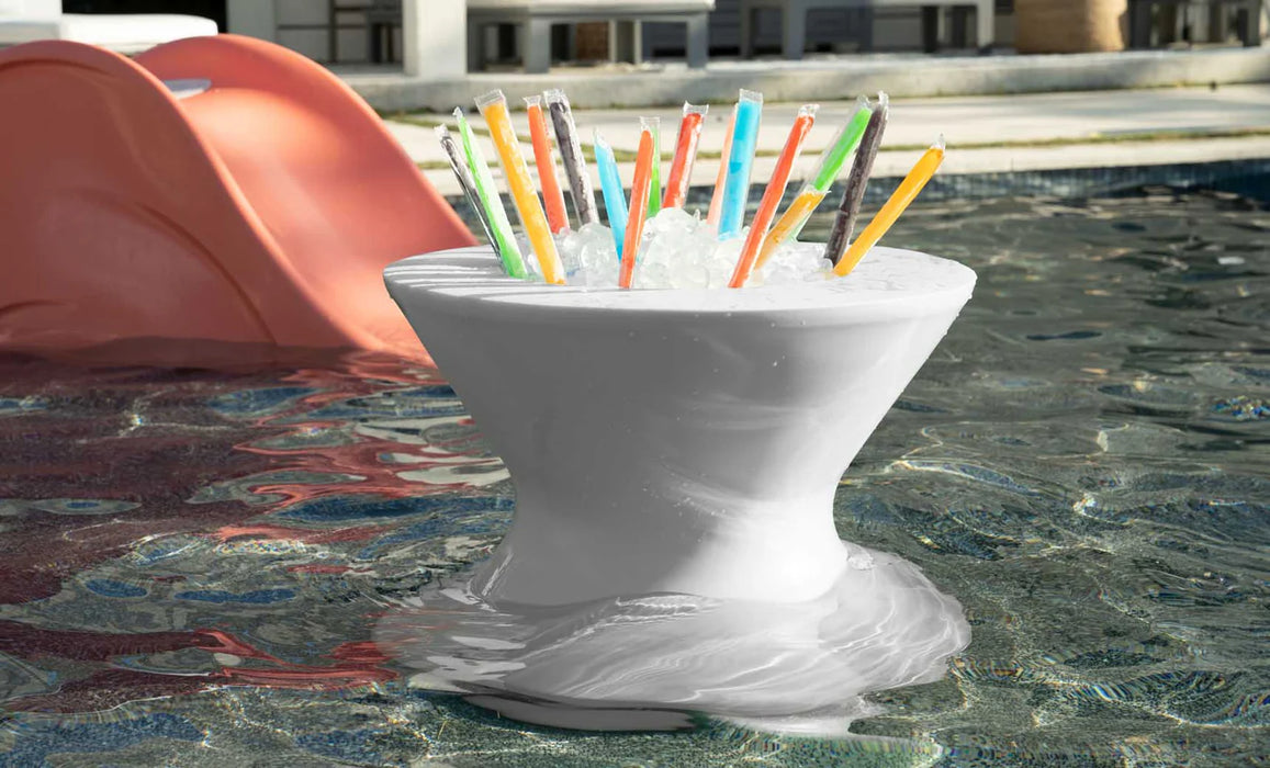 A photo showcasing the Ledge Lounger Signature Tall Ice Bin Side Table in action. The table is floating in a pool and filled with ice and a variety of popsicles, highlighting its functionality and style.