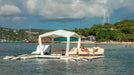 Floating platform with canopy on water, people sitting, and scenic background