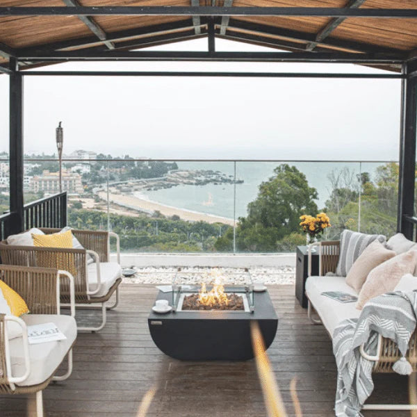 beautiful coastline view from balcony where there is a square fire pit table with other outdoor lounge furniture next to it