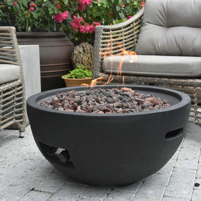 dark grey round fire pit bowl is burning on lava rocks in outside patio