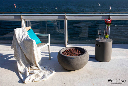 round propane fire bowl with matching tank cover being used as a convenient table top holding vase of flowers, fruit and wine in outside balcony