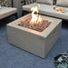 square fire pit table with lava rock. lava rocks are lit and there are yellow and orange flames