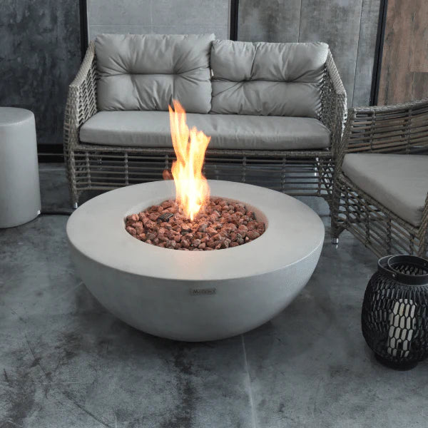 round fire pit table with fire pit lit on lava rocks next to patio furniture