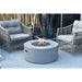 light grey round fire pit table. fire pit is lit on brown lava rocks and is in front of outdoor furniture