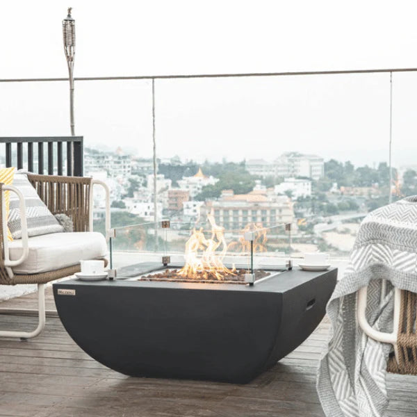 square fire pit table that is lit on lava rocks and shielded with glass windscreen on outdoor patio