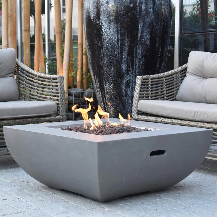 light grey square fire pit table is lit on brown lava rocks