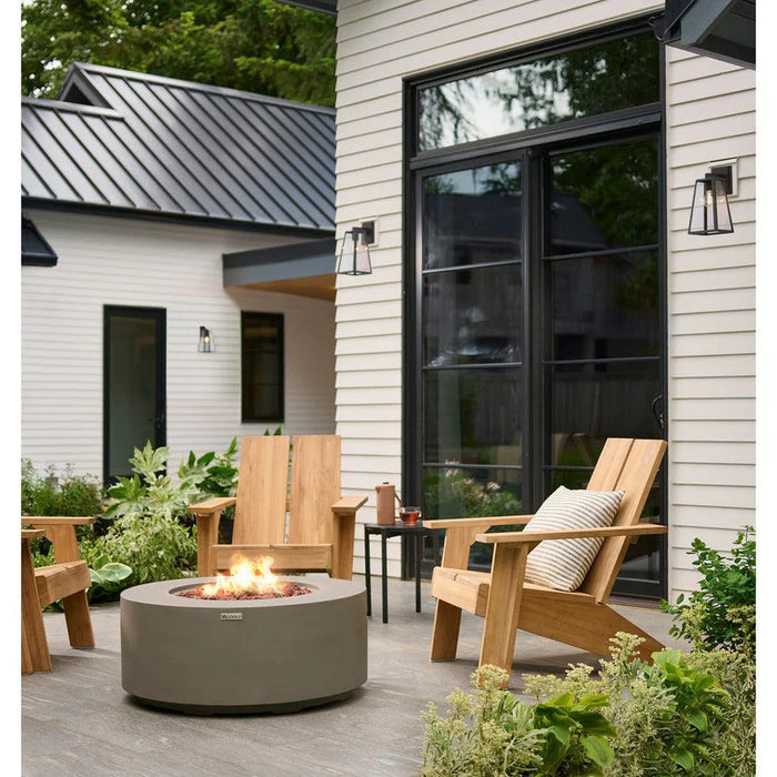 light grey round fire pit table is lit on lava rocks in front of wooden luxury chair beautifully set out in outdoor conservative